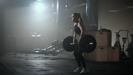 Female-bodybuilder-doing-exercise-with-weights-in-gym.-a-female-weightlifter-performs-a-barbell-lift-in-a-dark-gym.-Female-Bodybuilder-Does-Weight-Lift-Workout-Exercises-in-the-Hardcore-Training